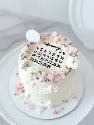 White minimalist calendar cake with pink and white icing flowers and a February calendar design. White minimalist calendar cake with pink and white icing flowers and a February calendar design.