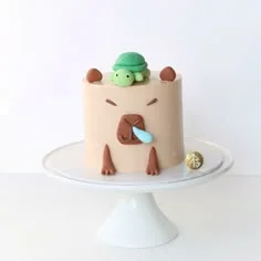 Capybara Silver Birthday Cake Tan capybara-themed cake with piped icing facial features and a small green turtle figurine on top