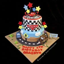 Cars-Inspired Birthday 2-Tier Cake Blue and checkered 2-tier fondant birthday cake with Cars characters, stars, and road accents