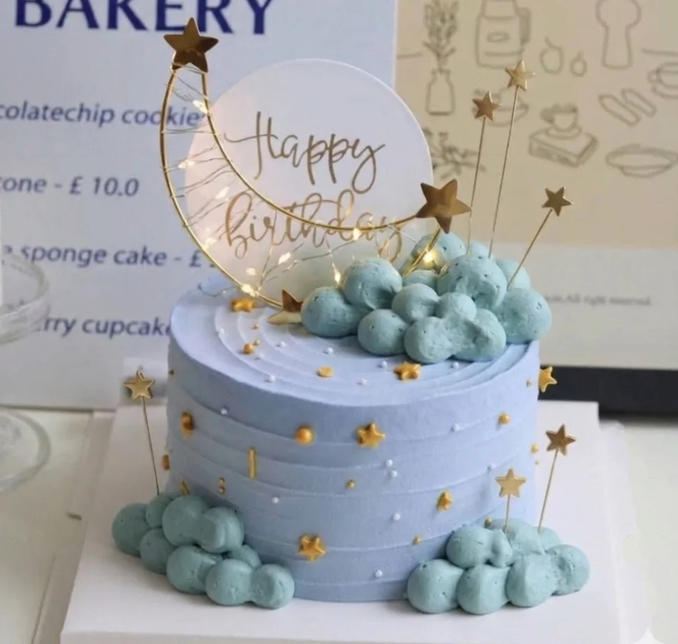 Light blue textured icing cake with gold stars, white clouds, and a moon topper with fairy lights. Light blue textured icing cake with gold stars, white clouds, and a moon topper with fairy lights.