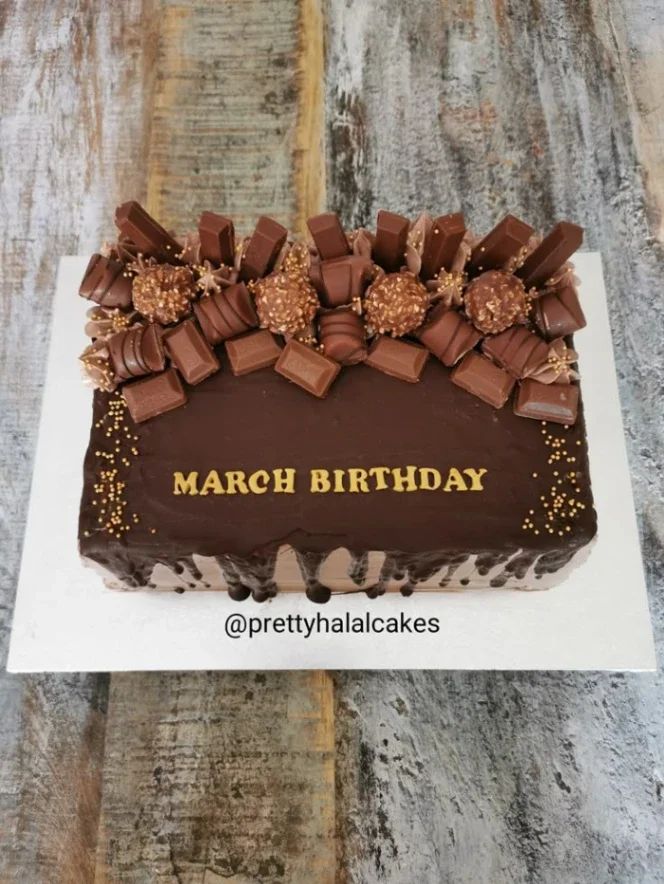 Chocolate rectangle cake with chocolate bar toppings, Ferrero Rocher, and gold sprinkles with a March Birthday message. Chocolate rectangle cake with chocolate bar toppings, Ferrero Rocher, and gold sprinkles with a March Birthday message.