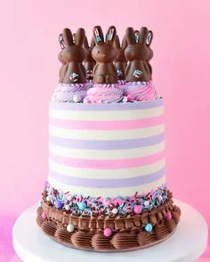 Tall striped pink and lavender cake topped with chocolate bunny figures and colorful sprinkles at the base. Tall striped pink and lavender cake topped with chocolate bunny figures and colorful sprinkles at the base.