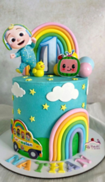 Cocomelon themed 1-tier birthday cake with JJ figure, rainbow, and yellow school bus on a blue icing base with clouds and stars. Cocomelon themed 1-tier birthday cake with JJ figure, rainbow, and yellow school bus on a blue icing base with clouds and stars.