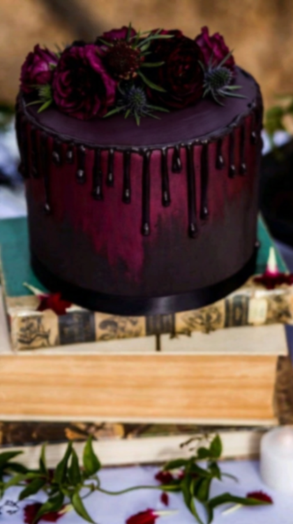 A dark red and black ombre 1-tier cake, featuring dark red and purple roses, dark chocolate drip, and thistle accents.