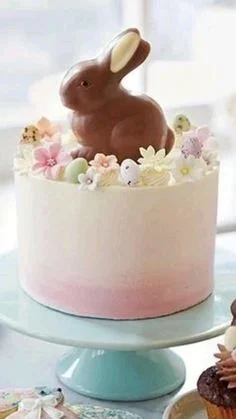 A single tier white and pink gradient cake topped with a large chocolate bunny, pastel flowers, and mini Easter eggs. A single tier white and pink gradient cake topped with a large chocolate bunny, pastel flowers, and mini Easter eggs.