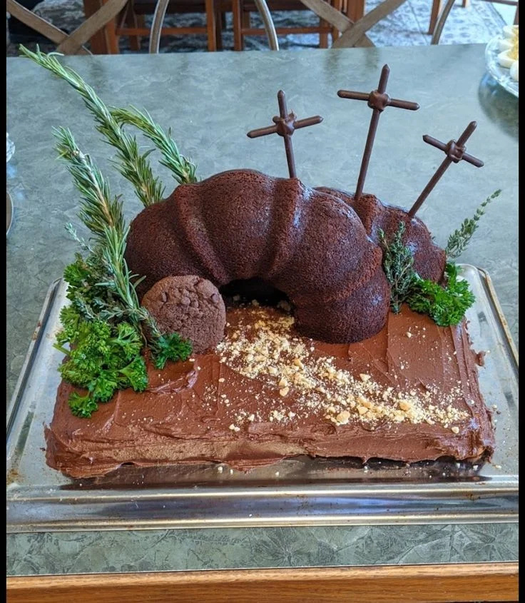 A chocolate rectangle cake designed as an empty tomb with three chocolate crosses and fresh rosemary and parsley greenery. A chocolate rectangle cake designed as an empty tomb with three chocolate crosses and fresh rosemary and parsley greenery.
