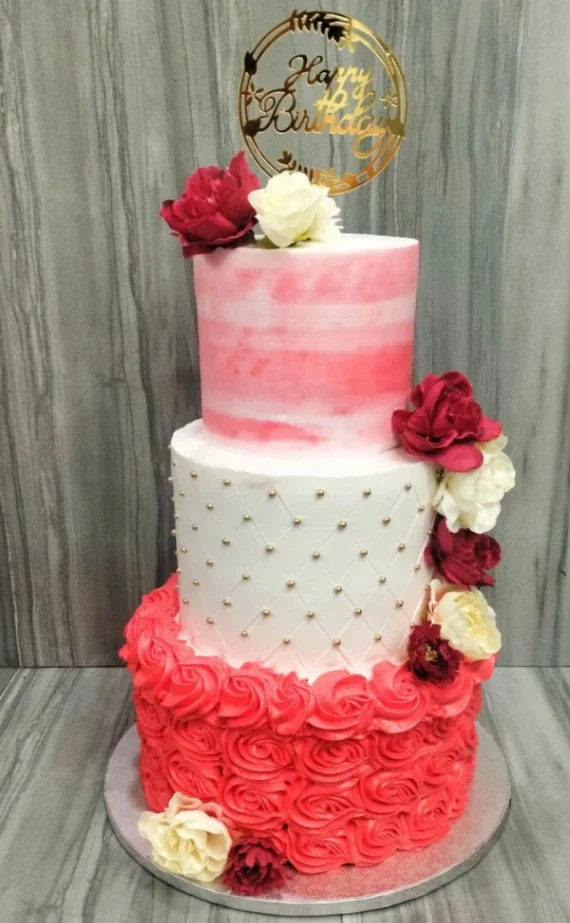 Elegant three-tier birthday cake with pink watercolor top tier, white quilted middle tier with gold dragees, and red rose-piped bottom tier. Elegant three-tier birthday cake with pink watercolor top tier, white quilted middle tier with gold dragees, and red rose-piped bottom tier.