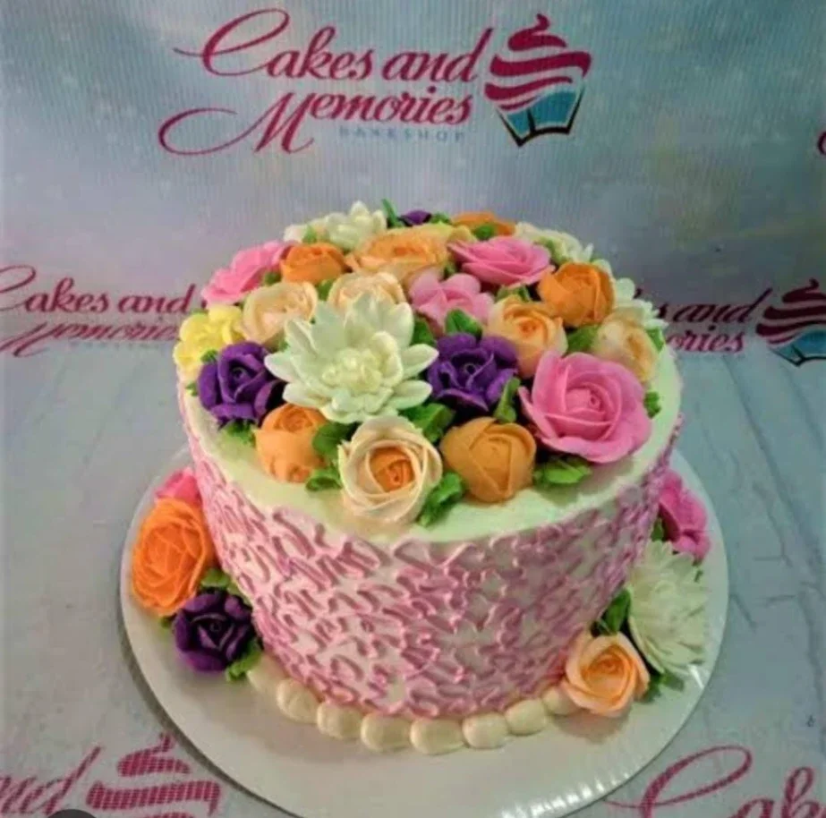 A single-tier white cake covered in a dense arrangement of colorful icing roses in pink, orange, purple, and white with green leaves. A single-tier white cake covered in a dense arrangement of colorful icing roses in pink, orange, purple, and white with green leaves.