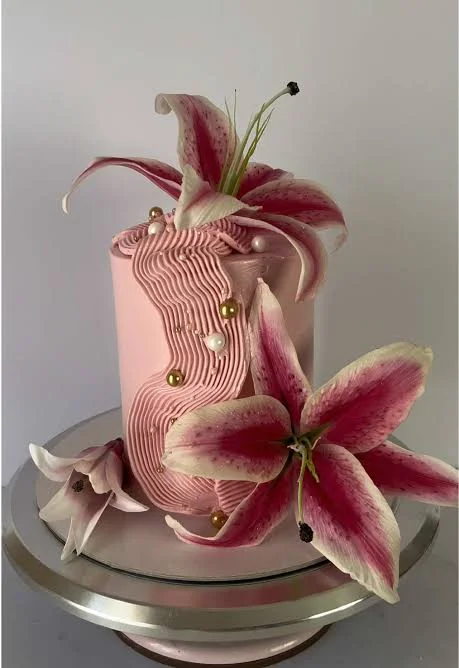 Floral Lily Pink Cake Soft pink 1-tier cake with smooth icing, large sculpted stargazer lilies, and gold pearl dragees