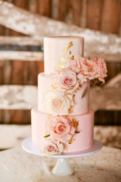 Elegant three-tier light pink fondant wedding cake decorated with cascading fresh peach and pink roses and gold leaf accents. Elegant three-tier light pink fondant wedding cake decorated with cascading fresh peach and pink roses and gold leaf accents.