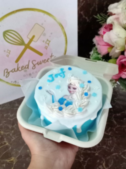 Frozen-Inspired Bento White Cake Sky blue bento cake with soft icing, a white drip, an Elsa edible photo topper, and piped blue snowflakes