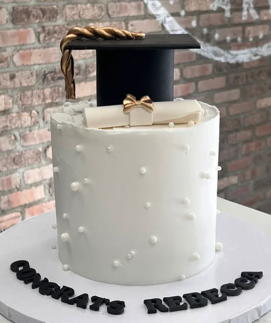 Tall white graduation cake with a black fondant graduation cap, a white gumpaste diploma with a gold bow, and white pearl sprinkles. Tall white graduation cake with a black fondant graduation cap, a white gumpaste diploma with a gold bow, and white pearl sprinkles.