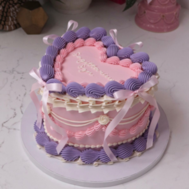 Heart Vintage Pink Cake Light pink heart vintage cake with smooth soft icing, piped purple shell borders, and pink ribbon bows