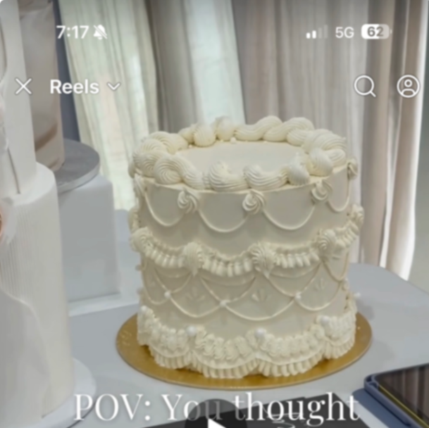 Elegant ivory vintage-style cake with intricate piped ruffles, swags, and pearl accents on a gold base. Elegant ivory vintage-style cake with intricate piped ruffles, swags, and pearl accents on a gold base.