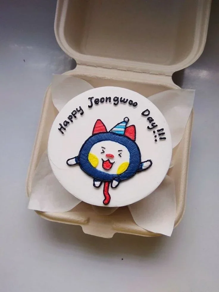 White bento cake with a hand-piped blue character wearing a party hat and the message Happy Jeongwoo Day White bento cake with a hand-piped blue character wearing a party hat and the message Happy Jeongwoo Day
