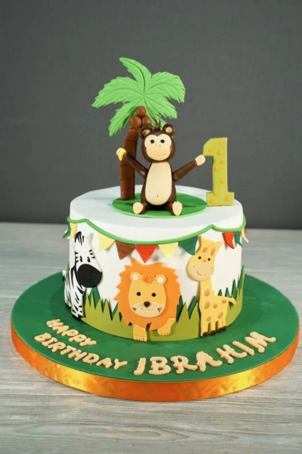 White fondant jungle themed cake with a 3D monkey topper, palm tree, and edible safari animals like a lion, zebra, and giraffe on the side. White fondant jungle themed cake with a 3D monkey topper, palm tree, and edible safari animals like a lion, zebra, and giraffe on the side.