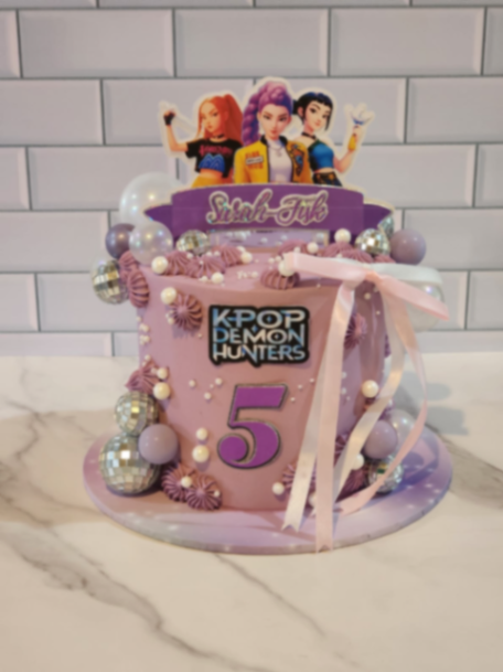 Purple K-Pop Demon Hunters themed cake with character printouts, disco balls, and a pink ribbon.