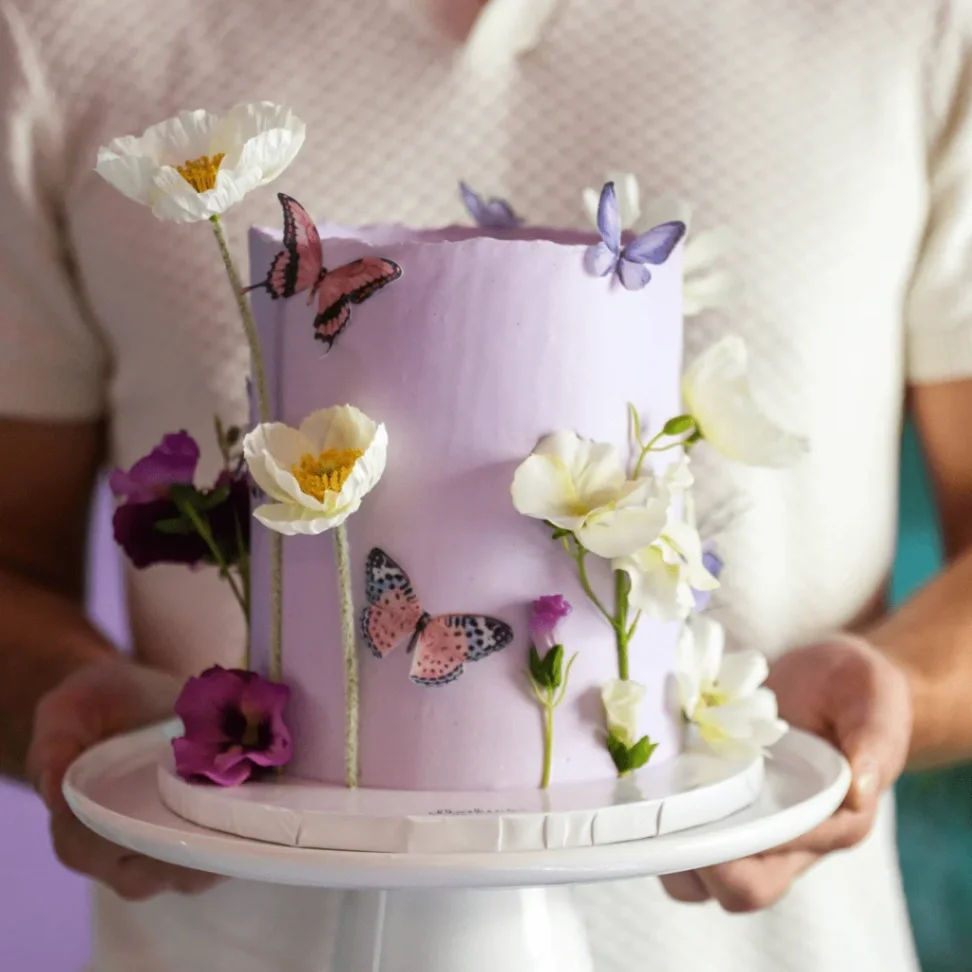 Lavender Butterfly Floral Cake Soft lavender 1-tier cake with smooth icing, lavender butterfly theme, and white and purple edible flowers