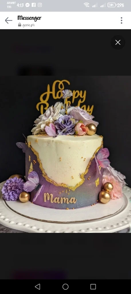 A tall purple and white cake for Mama featuring gold-edged icing, butterflies, and floral toppers. A tall purple and white cake for Mama featuring gold-edged icing, butterflies, and floral toppers.