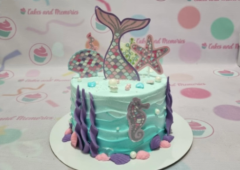 Light blue mermaid themed cake with a large mermaid tail topper, starfish, and purple seaweed icing decorations.