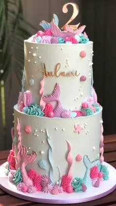 Two-tier light blue mermaid themed cake with pink and teal icing swirls, mermaid tails, and a gold number two topper. Two-tier light blue mermaid themed cake with pink and teal icing swirls, mermaid tails, and a gold number two topper.