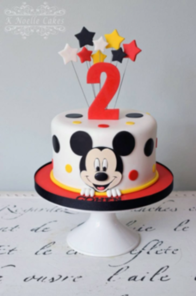 Mickey Mouse-Inspired White Birthday Cake White fondant cake with a Mickey Mouse face panel, red number two topper, and colorful star accents