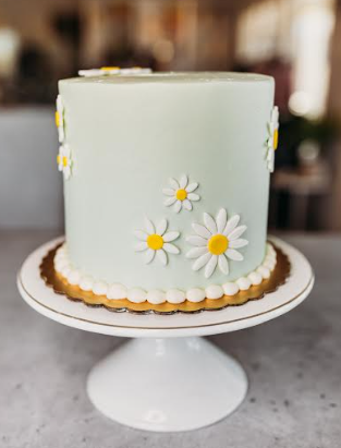 Tall mint green cake decorated with white and yellow fondant daisies and a white pearl border on a gold base. Tall mint green cake decorated with white and yellow fondant daisies and a white pearl border on a gold base.