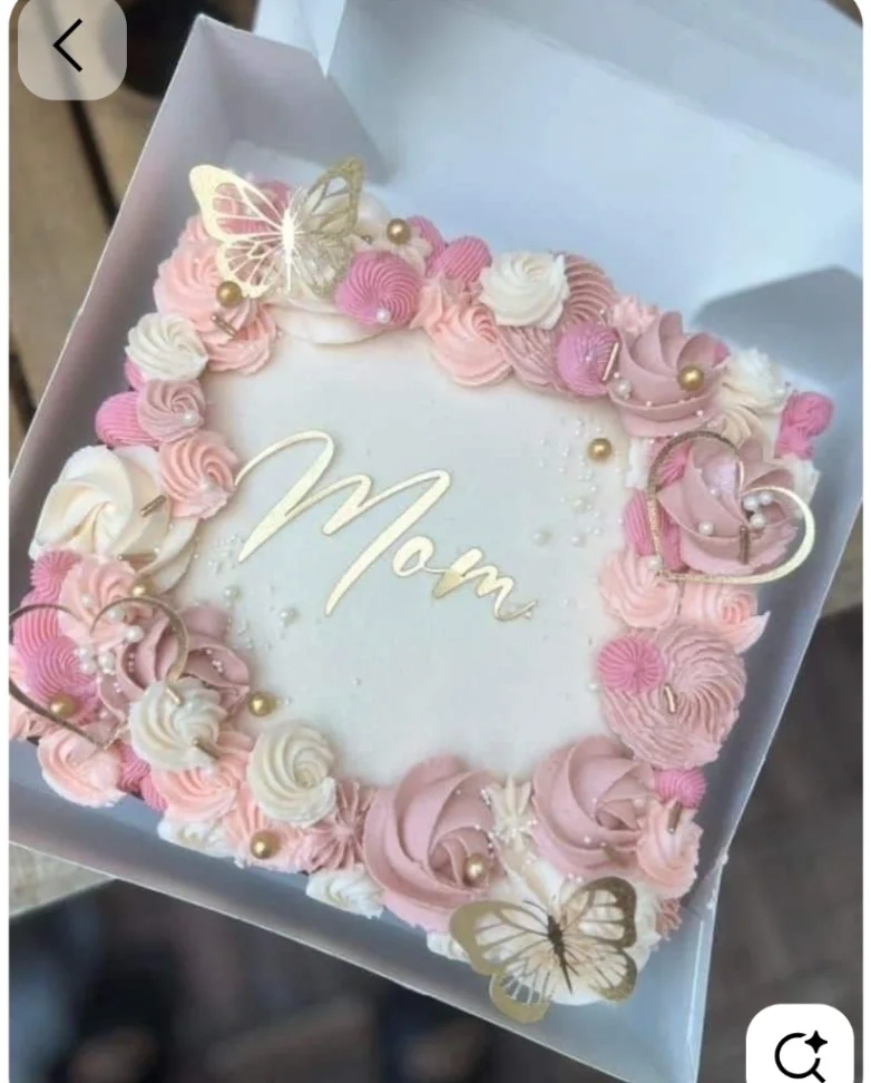 Square white cake with pink and ivory icing rosettes, gold butterflies, and a gold Mom topper.