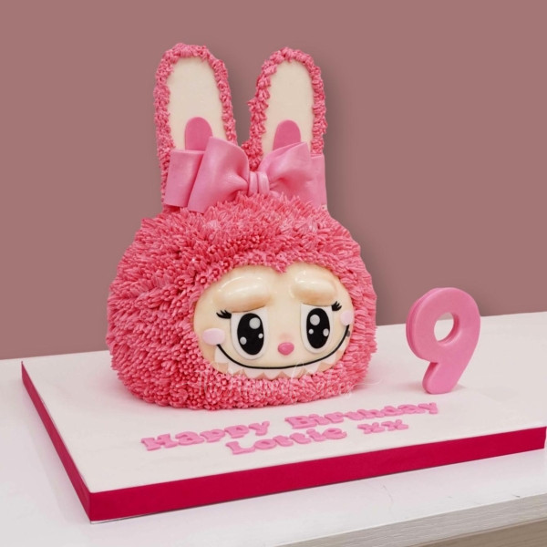 Pink furry monster cake with bunny ears, a pink bow, and a large number 9 topper on a white baseboard. Pink furry monster cake with bunny ears, a pink bow, and a large number 9 topper on a white baseboard.
