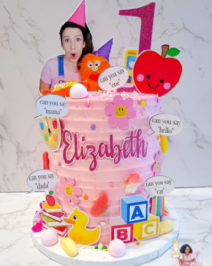 Pink Ms. Rachel themed birthday cake with character printouts, alphabet blocks, and colorful fondant accents. Pink Ms. Rachel themed birthday cake with character printouts, alphabet blocks, and colorful fondant accents.