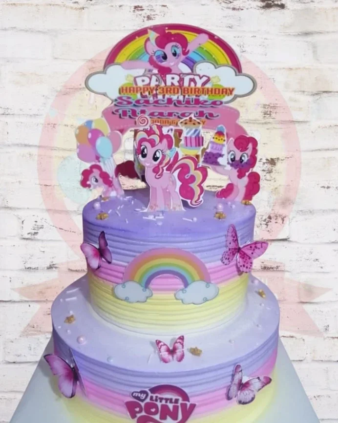 Two-tier My Little Pony themed birthday cake with purple and yellow gradient icing, rainbow printouts, and Pinkie Pie character toppers. Two-tier My Little Pony themed birthday cake with purple and yellow gradient icing, rainbow printouts, and Pinkie Pie character toppers.