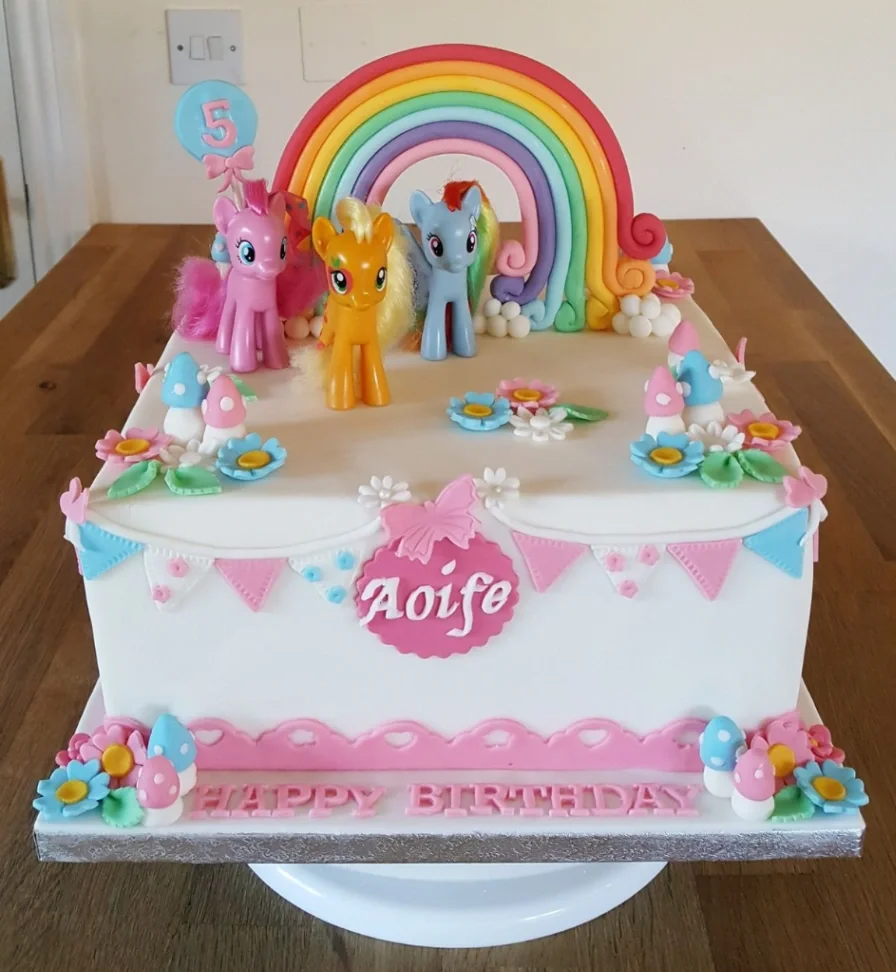 White rectangle fondant cake with My Pony figurines, a large fondant rainbow, and colorful gumpaste flowers and mushrooms. White rectangle fondant cake with My Pony figurines, a large fondant rainbow, and colorful gumpaste flowers and mushrooms.