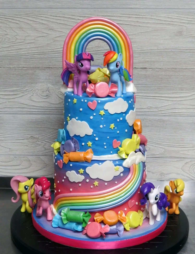Two-tier My Little Pony themed fondant cake with a large rainbow topper, edible clouds, and colorful candy decorations. Two-tier My Little Pony themed fondant cake with a large rainbow topper, edible clouds, and colorful candy decorations.