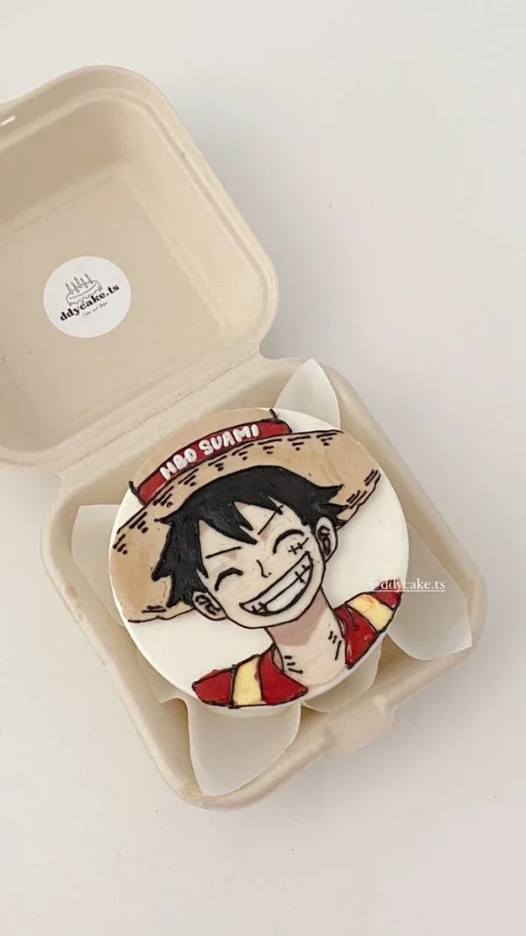 Bento cake featuring a hand-piped icing illustration of Monkey D. Luffy from One Piece with a red banner message. Bento cake featuring a hand-piped icing illustration of Monkey D. Luffy from One Piece with a red banner message.
