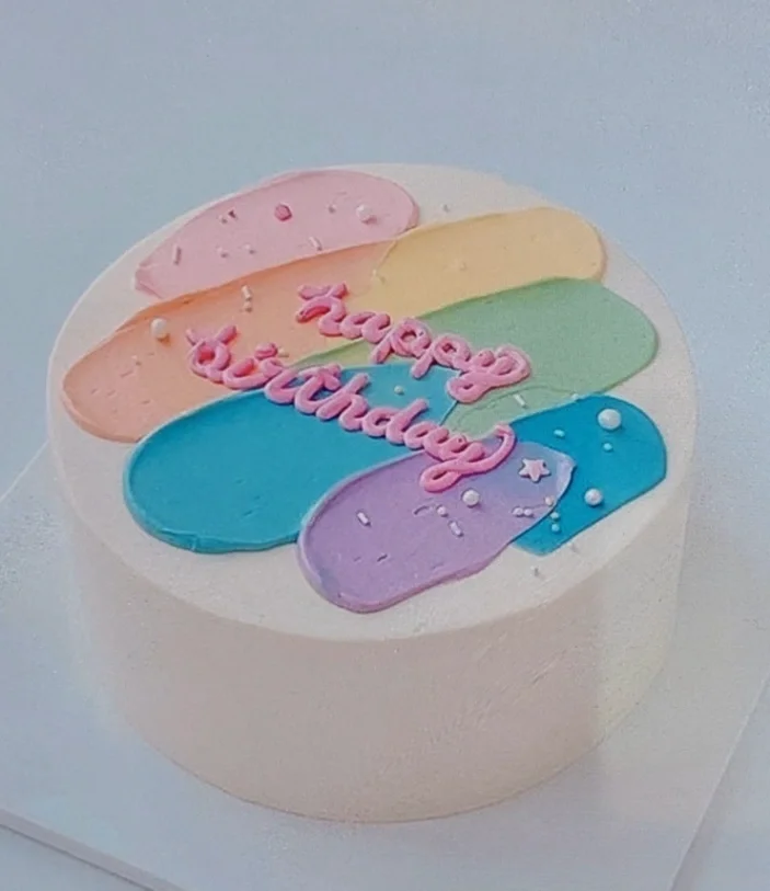 White minimalist bento-style cake with colorful pastel icing palette knife strokes and pink piped Happy Birthday message.