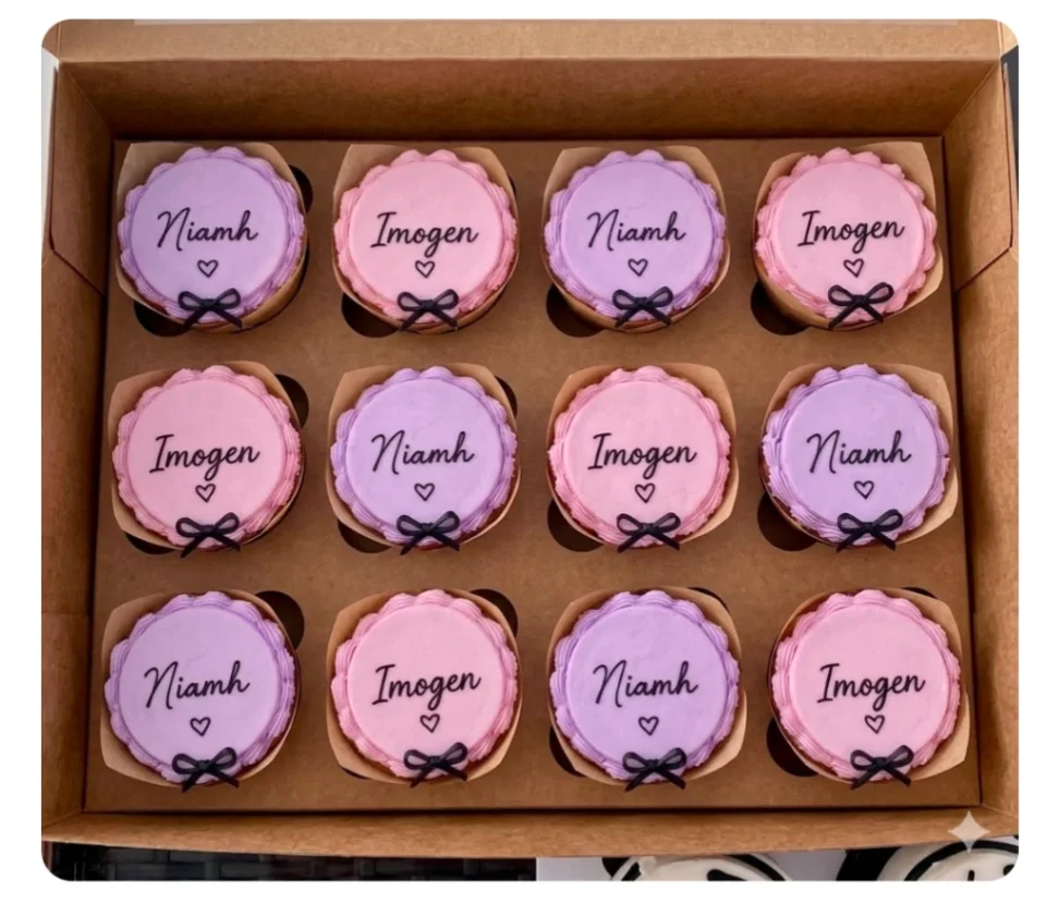 Personalized Cupcakes Lavender and pink cupcakes in a box with piped frosting borders, black script names, and tiny black ribbon bows