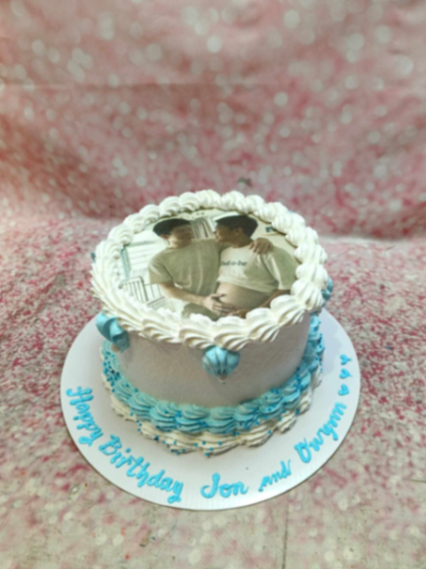 White and blue birthday cake with a photo print of a couple on top and blue icing rosettes. White and blue birthday cake with a photo print of a couple on top and blue icing rosettes.