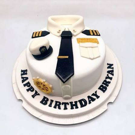 White fondant pilot uniform cake with black tie, captain hat, epaulettes, and gold anchor details on a white baseboard.