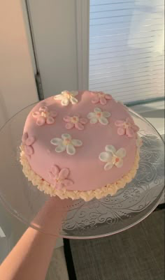 A single-tier pink cake decorated with white and pink icing flowers and a ruffled cream-colored base border. A single-tier pink cake decorated with white and pink icing flowers and a ruffled cream-colored base border.