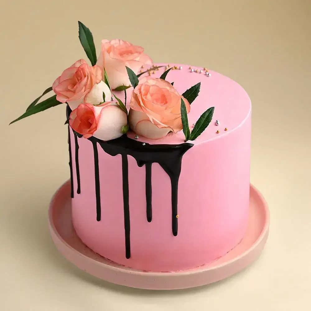 Pink Rose Drip Cake Pink 1-tier cake with smooth soft icing, a dark chocolate drip, and a cluster of fresh peach roses on top with silver and gold sprinkle accents