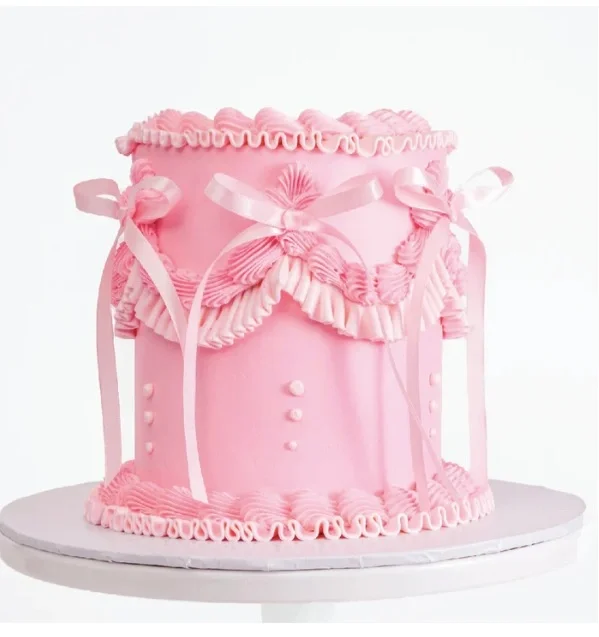 Tall pink vintage-style cake with intricate icing ruffles, piped borders, and light pink satin ribbons. Tall pink vintage-style cake with intricate icing ruffles, piped borders, and light pink satin ribbons.