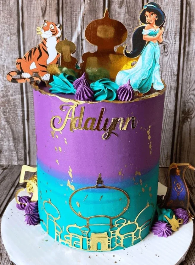 Tall purple and teal gradient cake with Princess Jasmine and Rajah printouts, gold palace silhouettes, and purple icing swirls. Tall purple and teal gradient cake with Princess Jasmine and Rajah printouts, gold palace silhouettes, and purple icing swirls.
