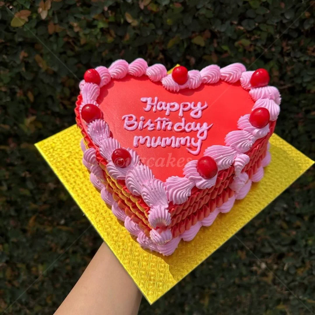 Heart-shaped red cake with pink piped icing borders and red cherry-like candy toppers on a gold base. Heart-shaped red cake with pink piped icing borders and red cherry-like candy toppers on a gold base.