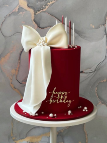 Tall dark red fondant cake with a large white gumpaste bow and gold Happy Birthday message. Tall dark red fondant cake with a large white gumpaste bow and gold Happy Birthday message.