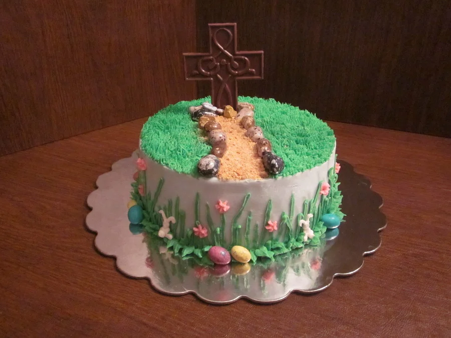 Religious Easter cake with a chocolate cross, stone path, green grass icing, and colorful eggs on a silver base. Religious Easter cake with a chocolate cross, stone path, green grass icing, and colorful eggs on a silver base.