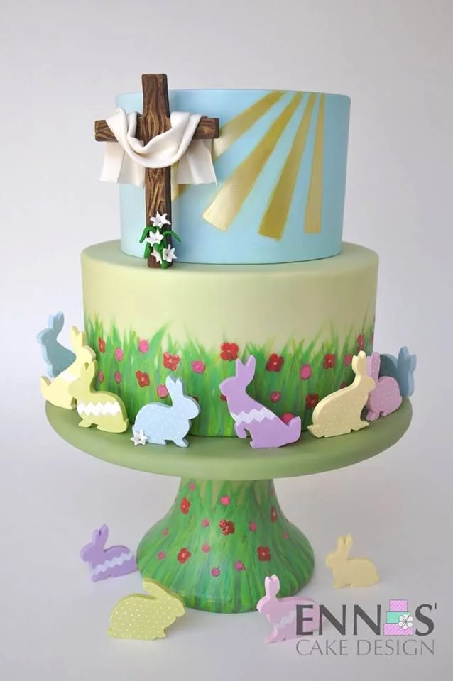 A two-tier religious Easter cake featuring a wooden cross with white fabric, golden sunbeams, and colorful fondant bunnies in a grass field. A two-tier religious Easter cake featuring a wooden cross with white fabric, golden sunbeams, and colorful fondant bunnies in a grass field.