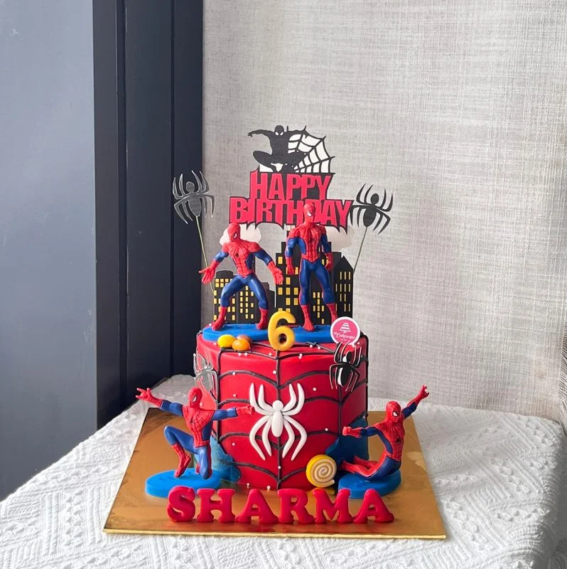 Red 1-tier fondant Spiderman birthday cake with action figures, city cardstock toppers, and black webbing Red 1-tier fondant Spiderman birthday cake with action figures, city cardstock toppers, and black webbing