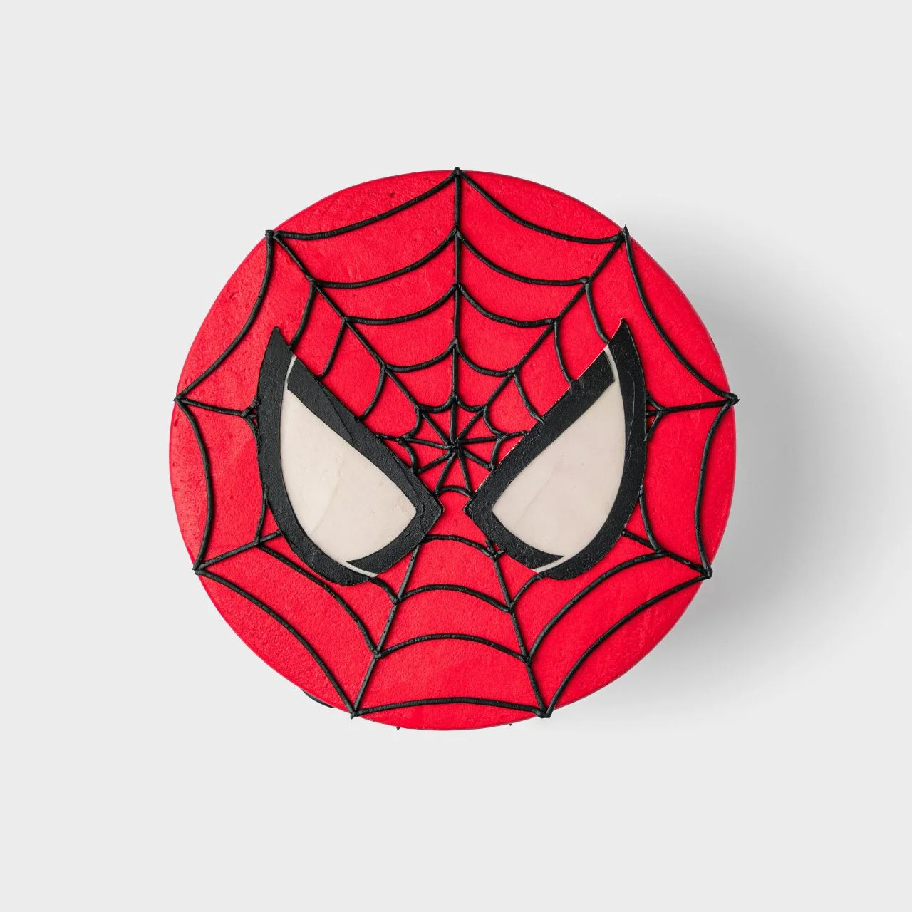 Spiderman-Inspired Birthday Cake Bright red 1-tier soft icing cake with black piped spider web lines and large white and black Spiderman eyes on top