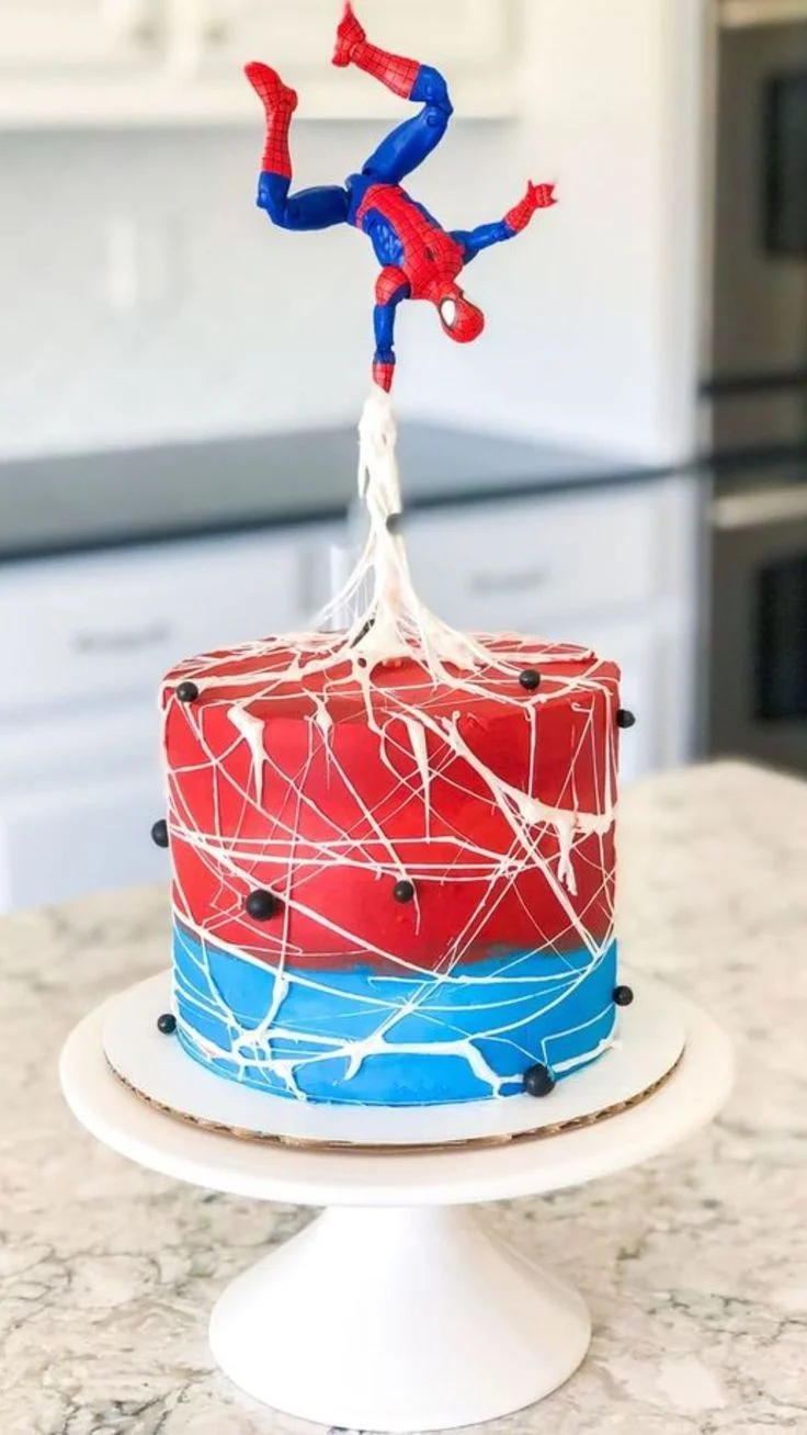 Spiderman-Inspired Birthday Cake Red and blue single-tier cake with soft icing, white piped webbing, and a Spider-Man action figure