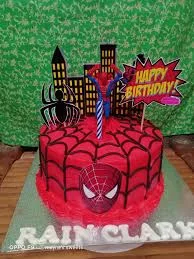 Red Spiderman themed birthday cake with black web icing, a Spiderman mask on the side, and city skyline toppers.